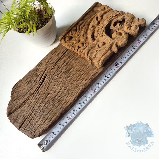 Wooden decorative piece with carvings on a white surface, accompanied by a measuring tape for scale.