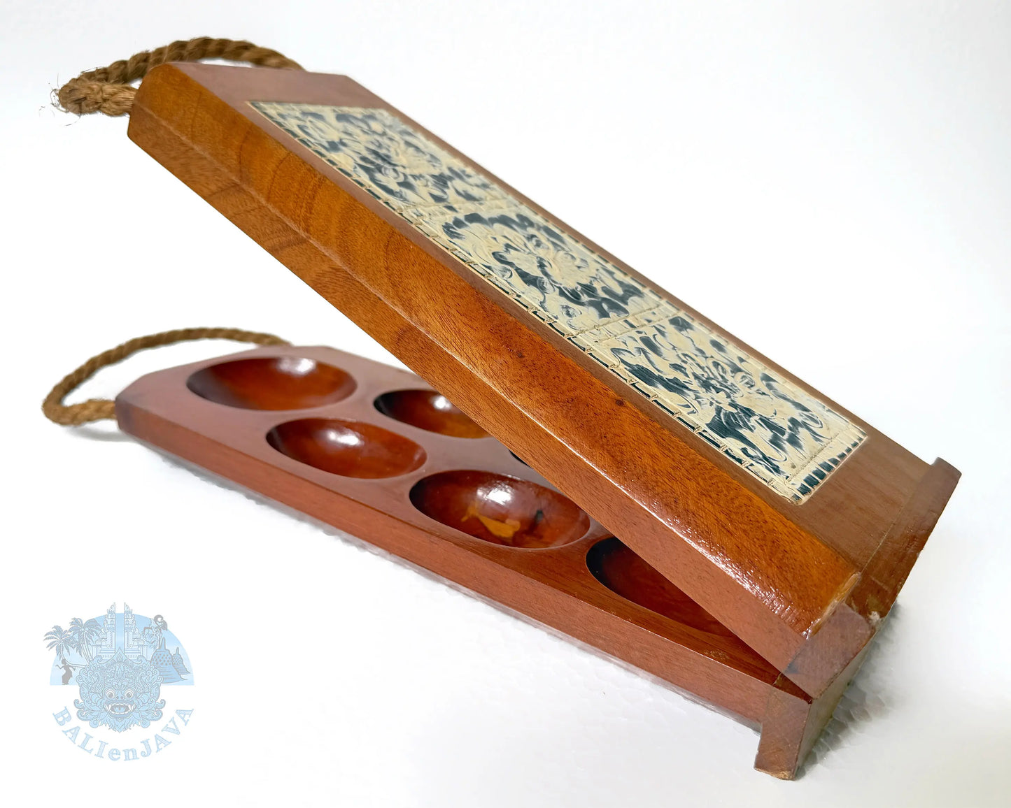 A wooden mancala game board set with a hinged lid, featuring oval holes and a decorative carved panel on the lid. The set is photographed on a plain white background with a small watermark in the lower-left corner.