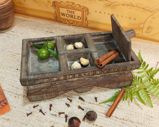 Wooden box with compartments containing limes, stones, and cinnamon sticks, on a textured surface with a world map in the background.