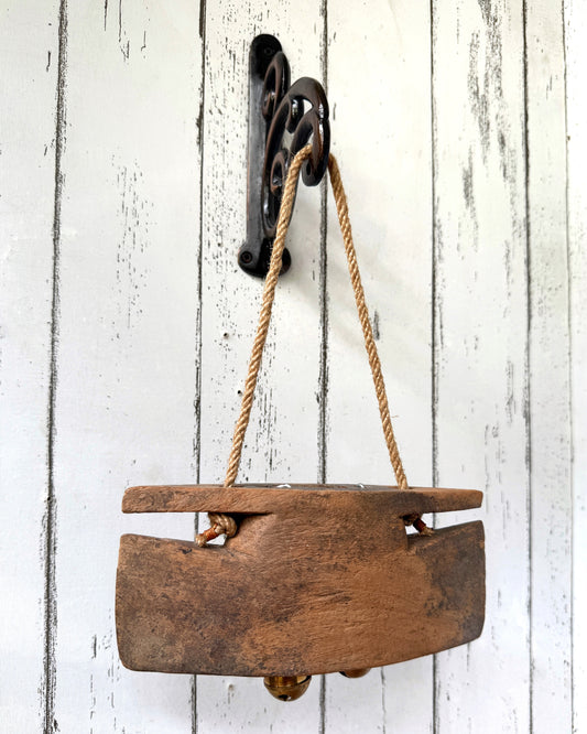 Wooden cattle bell hanging on wall hook on a white wooden wall