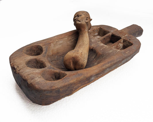 An old, hand-carved wooden mortar and pestle set with a traditional figure head on a white background.
