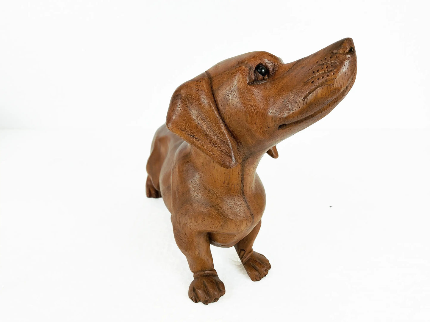 A wooden dachshund dog sculpture or figurine, shown from a three-quarters front view looking up, on a solid white background.