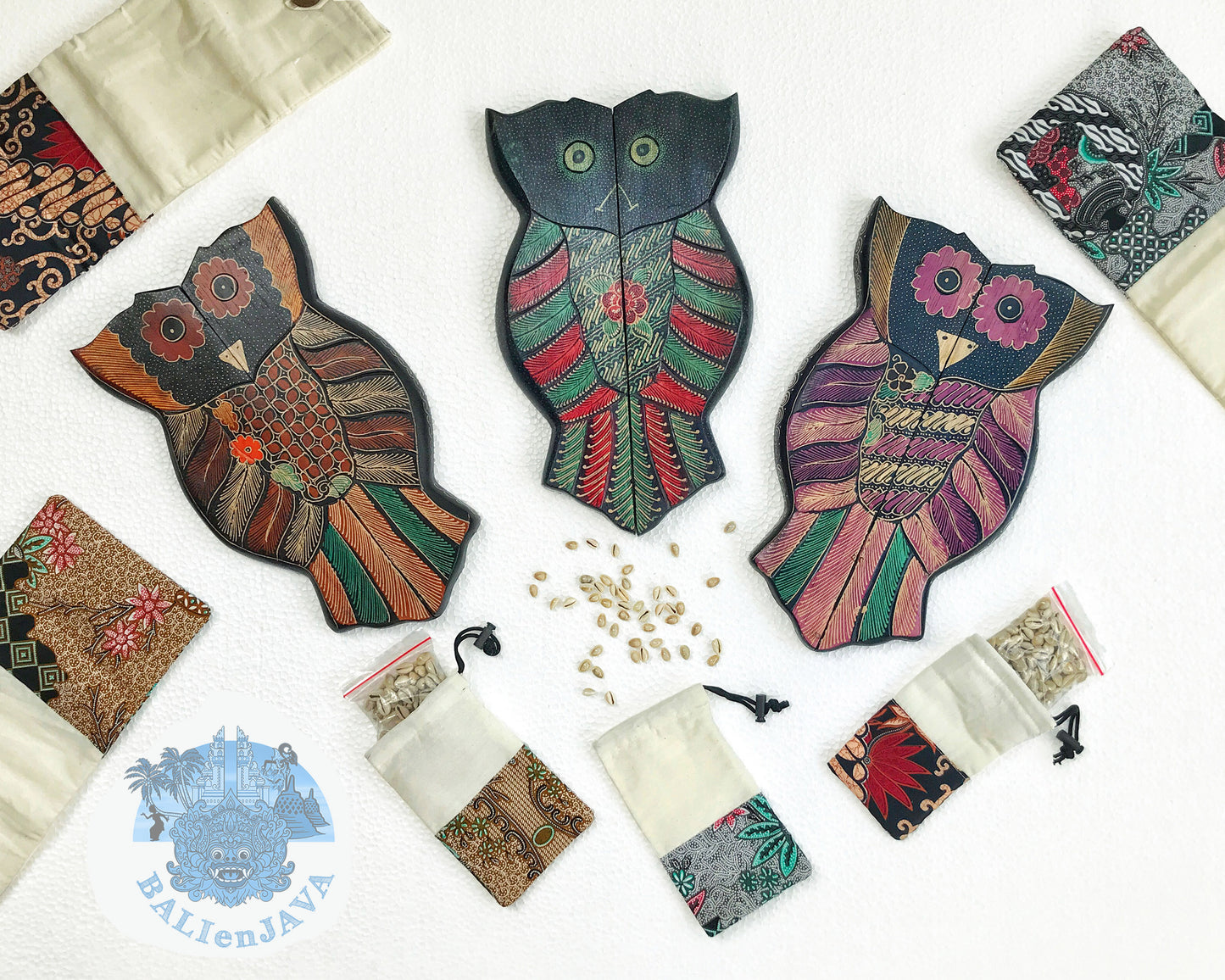 Colorful owl-shaped mancala games with patterned fabric bags and cowrie shells scattered on a white background.