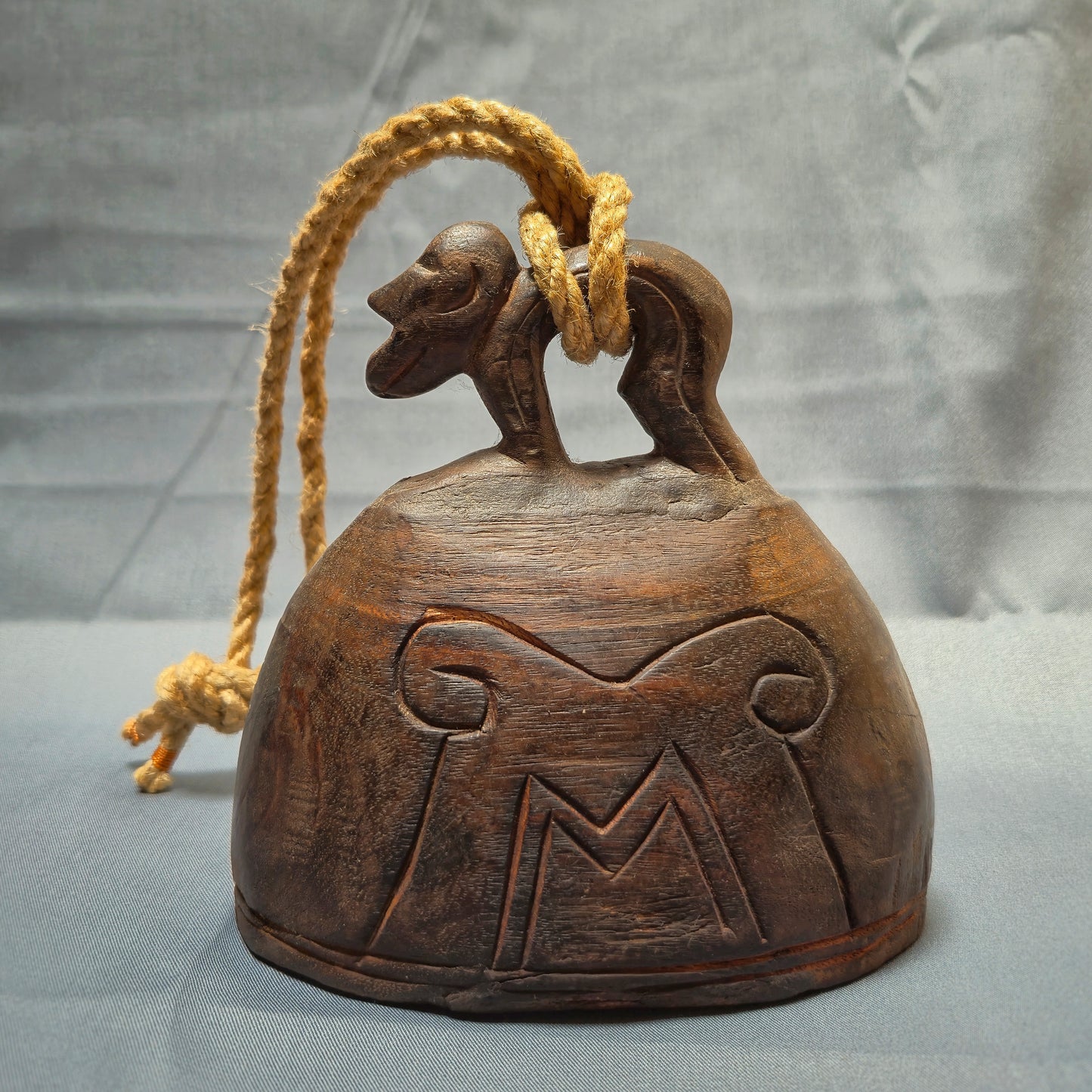 Wooden bell with rope and decorative carvings on a gray background
