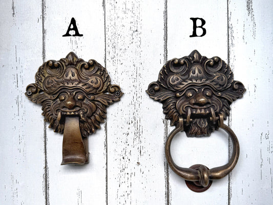 Two ornate bronze door knockers labeled A and B on a white wooden background.