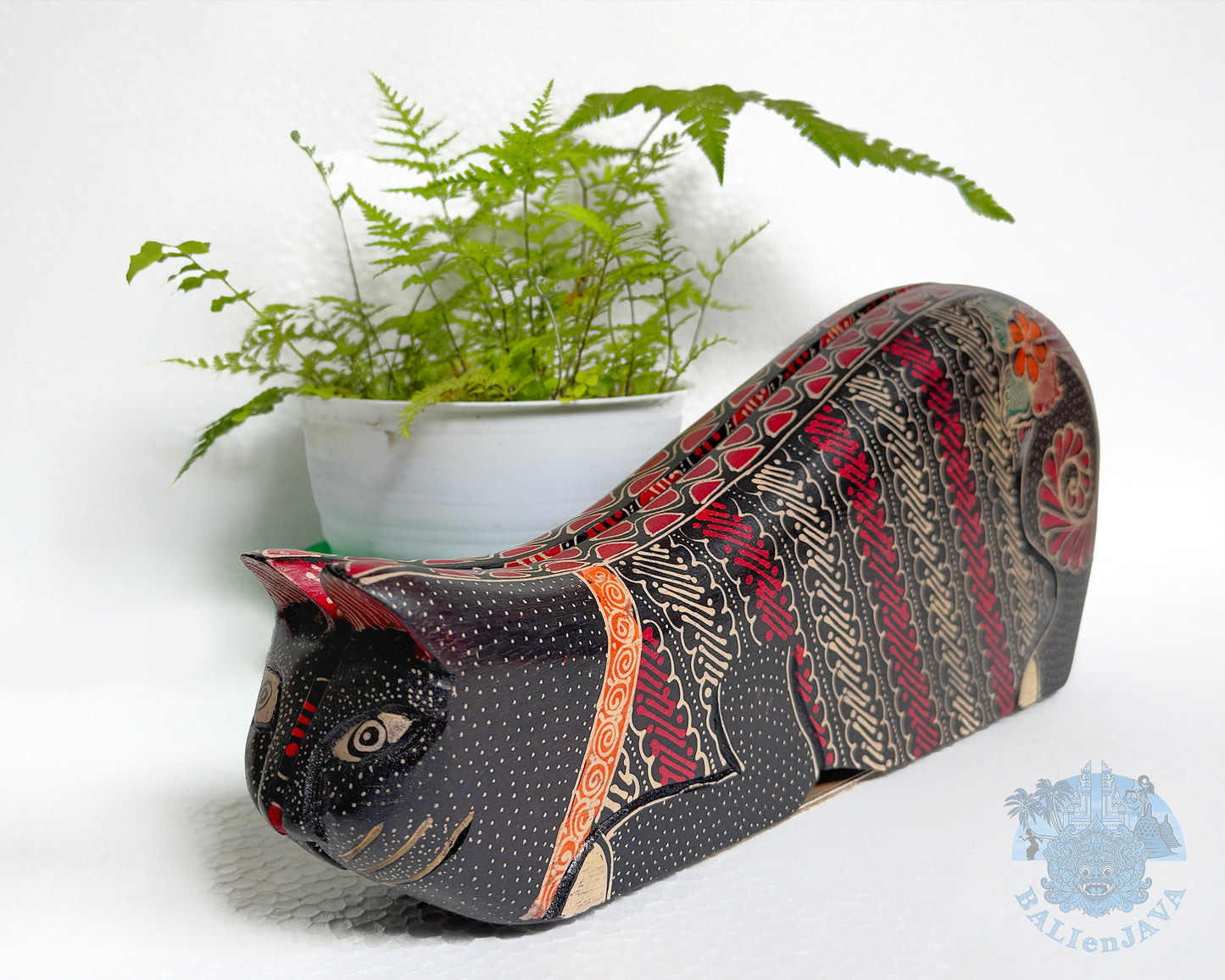 Decorative cat-shaped toy with intricate pattern next to a potted plant on a white background