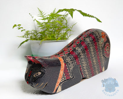 Decorative cat-shaped toy with intricate pattern next to a potted plant on a white background