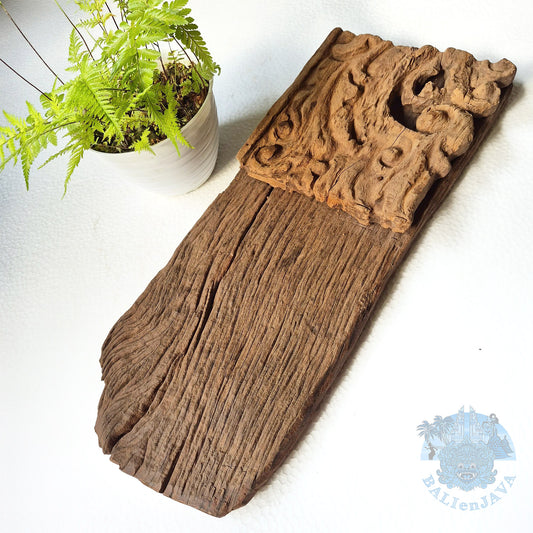 Wooden decorative wall hanging decor with carvings on a white surface next to a potted plant