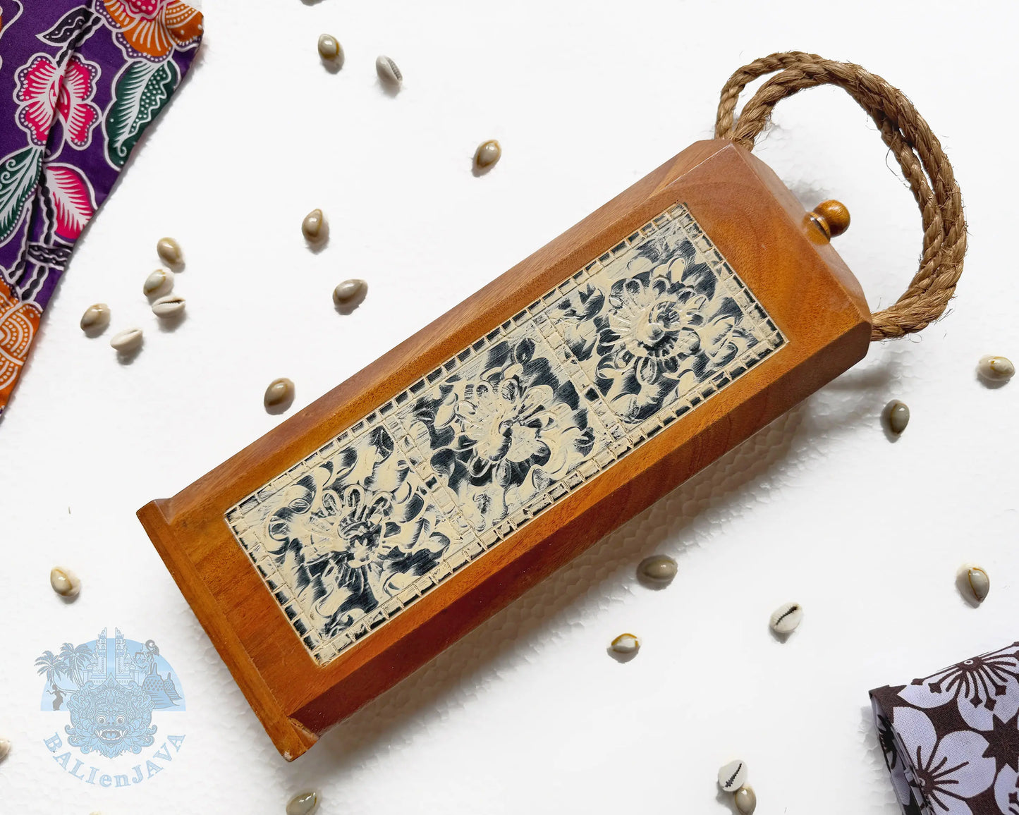 A rectangular wooden mancala board game with a hinged lid, a thick brown rope handle, featuring a central carved panel with floral patterns on a light beige background.