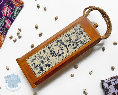 A rectangular wooden mancala board game with a hinged lid, a thick brown rope handle, featuring a central carved panel with floral patterns on a light beige background.
