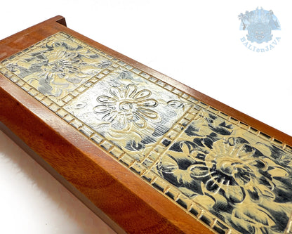 A close-up of a wooden box lid featuring a carved floral pattern with a warm brown wood frame.