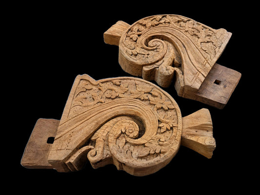 Two ornate Javanese carved wooden daybed legs with floral relief details, shown on a solid black background.