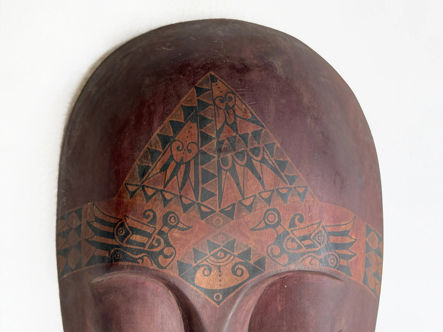 Decorative wooden mask with geometric tribal patterns on a white background