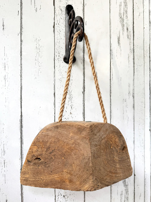 Wooden bell with a rope hanging on a rustic white wooden wall.