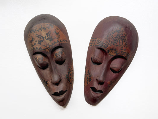 Two wooden masks with intricate carvings on a white background