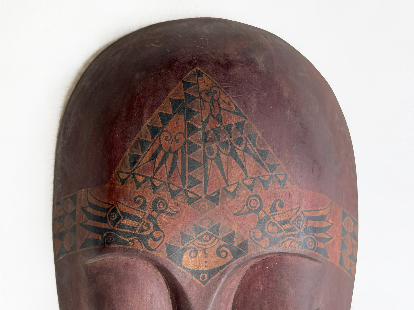 Decorative wooden mask with geometric patterns on a white background