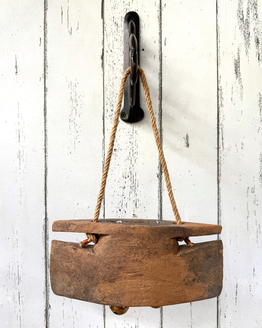 Vintage wooden bell hanging on a wall hook on a painted white wooden background