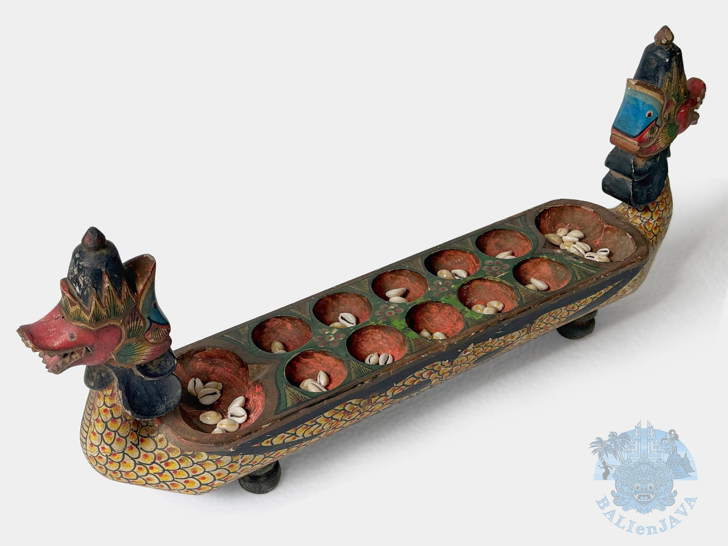 Decorative dragon-shaped board game with seashells in the holes on a white background