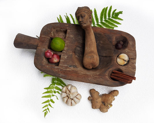 An old, hand-carved wooden mortar and pestle set with various spices and a traditional figure head on a white background.