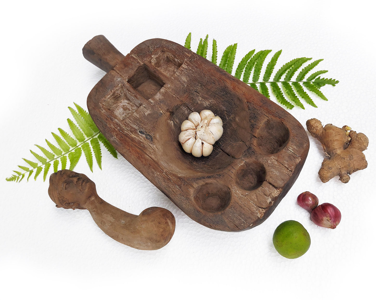 An old, hand-carved wooden mortar and pestle set with a traditional figure head on a white background.