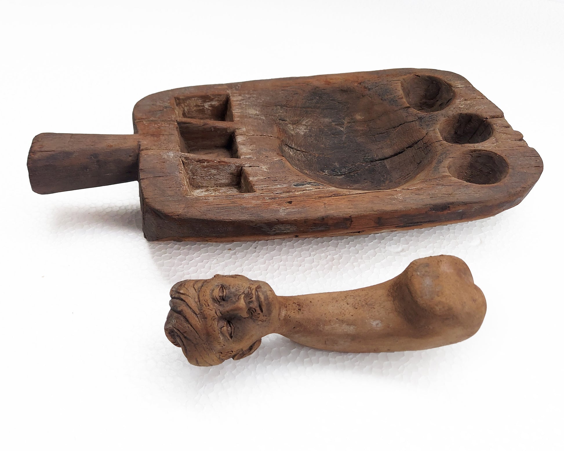An old, hand-carved wooden mortar and pestle set with a traditional figure head on a white background.