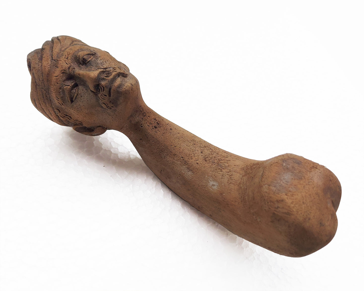 An old, hand-carved wooden mortar with the handle carved like a male face, positioned on a white background.