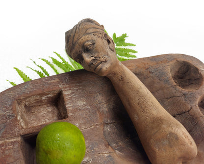 Close-up shot of an old, hand-carved wooden mortar with its handle carved like a male face, positioned on a wooden pestle. 