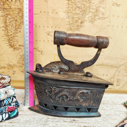 Vintage coal iron with dragon carving and wooden handle in front of an old world map background