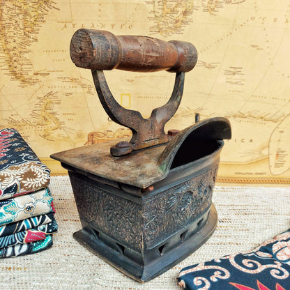 Vintage coal iron with wooden handle on a textured table cloth and and an old world map in the background