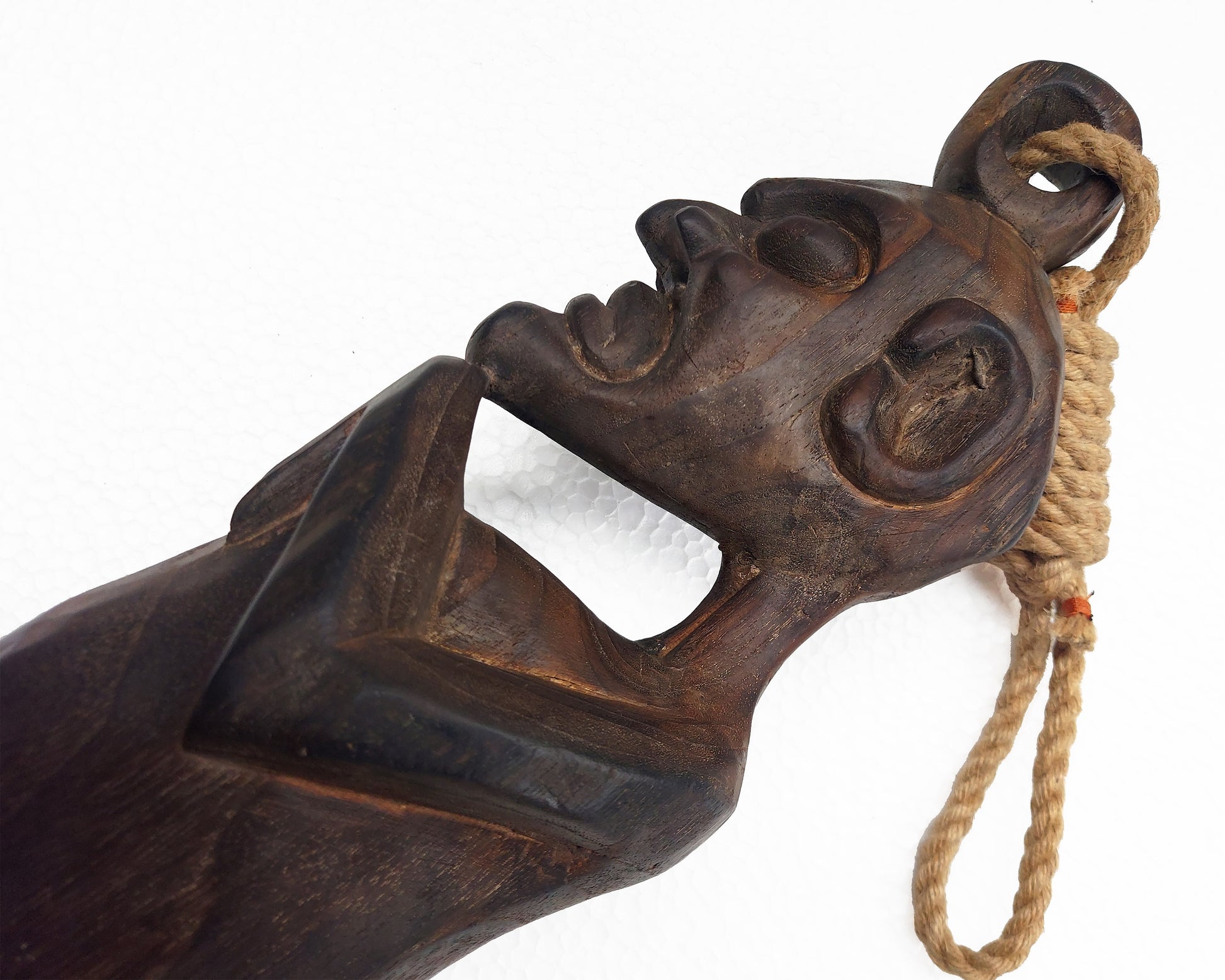 Carved wooden object with a face and rope on a white background