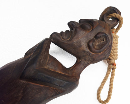 Carved wooden object with a face and rope on a white background