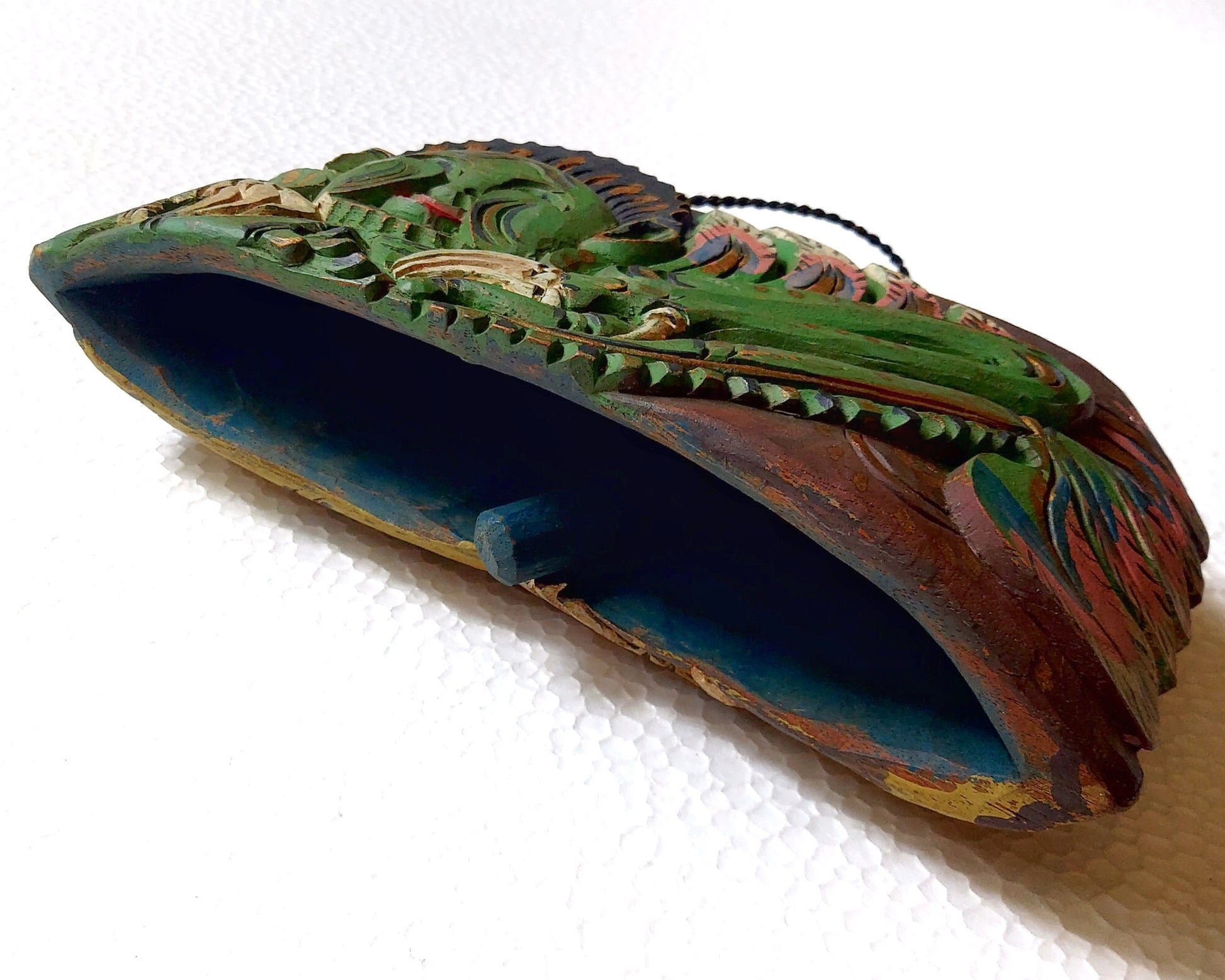 Bottom part of a wooden bell with carving of a green mythological creature with wooden clapper visible