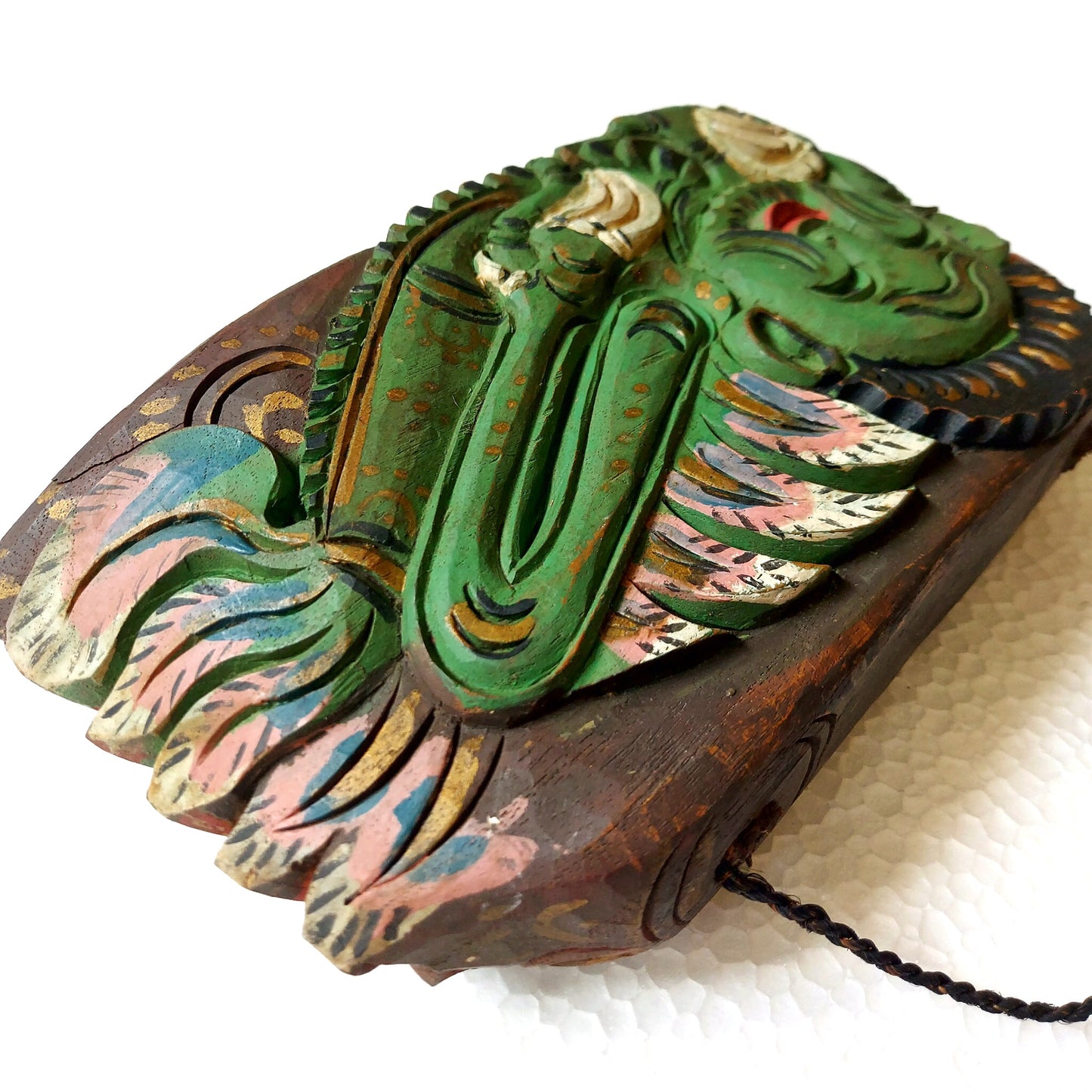 Close-up of a wooden bell with carving of a green mythological creature on a white surface