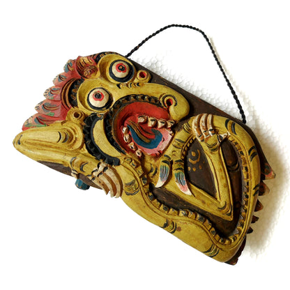 Wooden bell with carving of a yellow mythological creature and a rope handle on a white background
