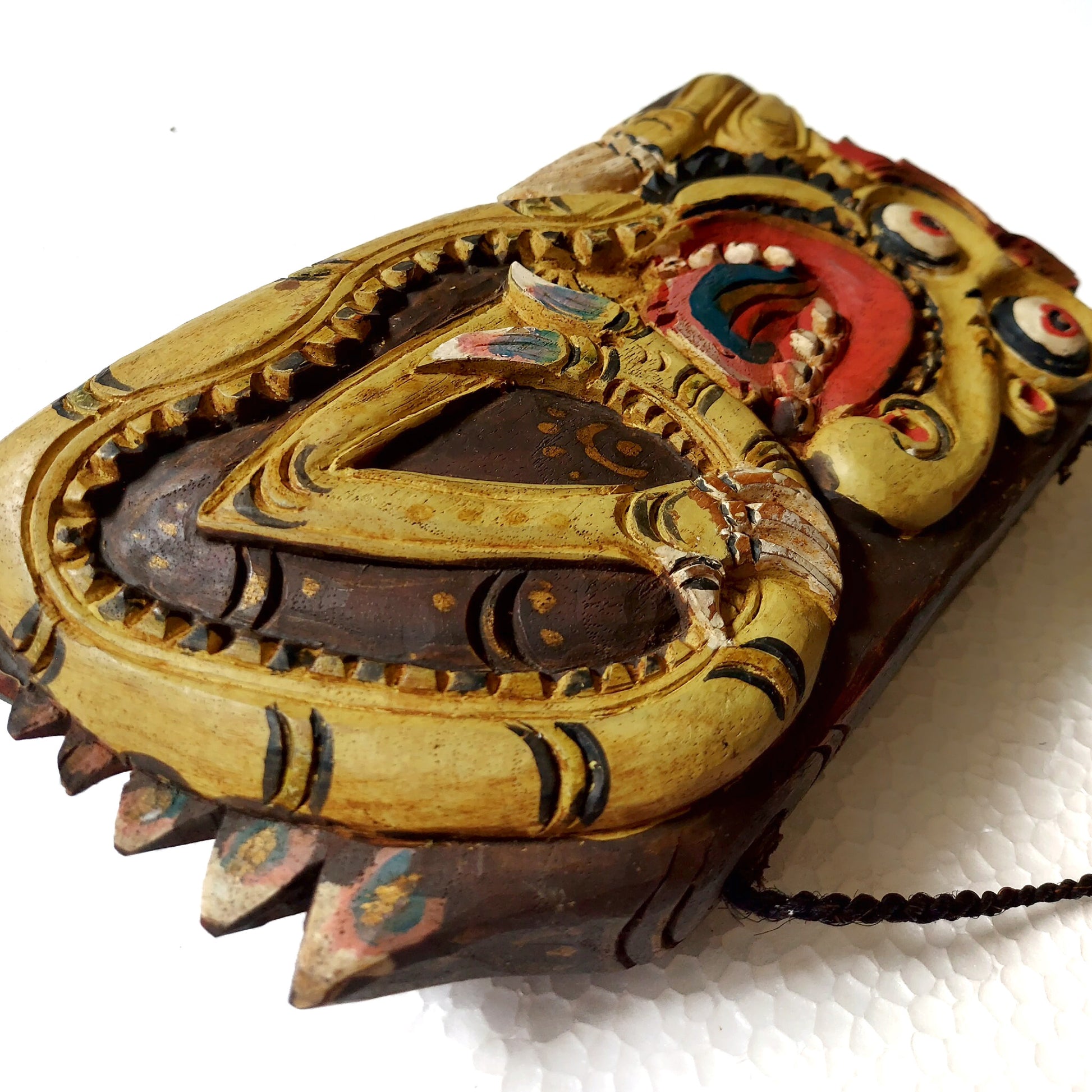 Close-up of a wooden bell with yellow colored mythological creature carving on a white background