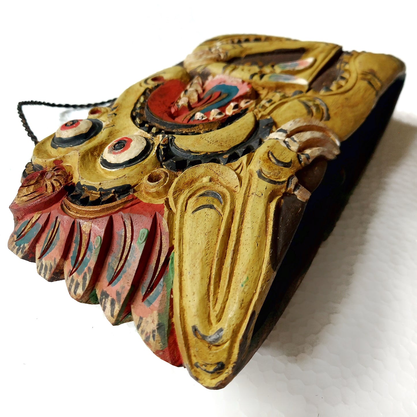 Close-up of a wooden bell with yellow colored mythological creature carving on a white background