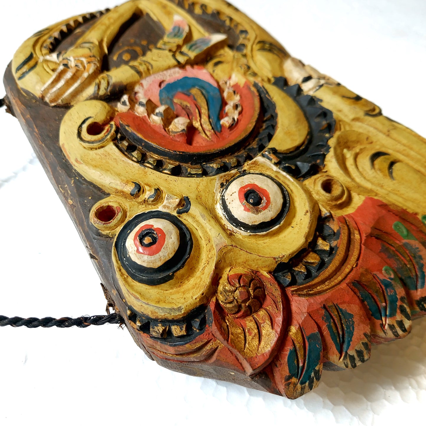 Close-up of a wooden bell with yellow colored mythological creature carving with large eyes on a white background