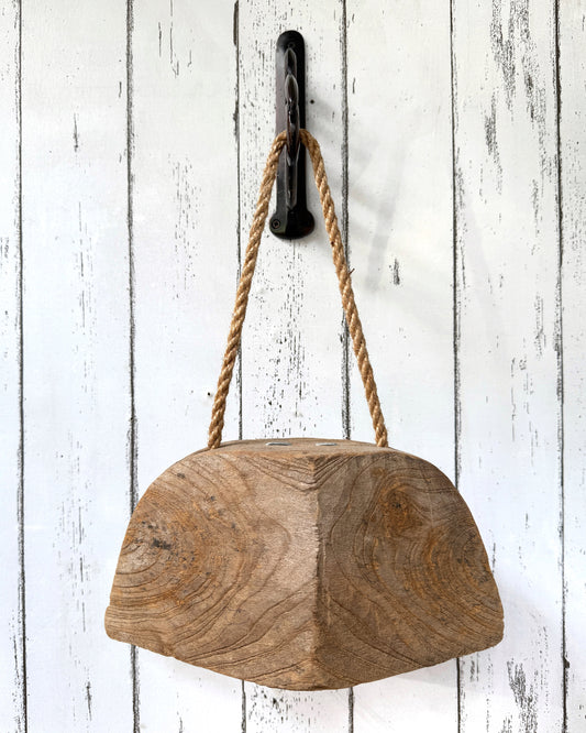 Wooden bell with rope handle hanging on hook attached to a white wooden wall