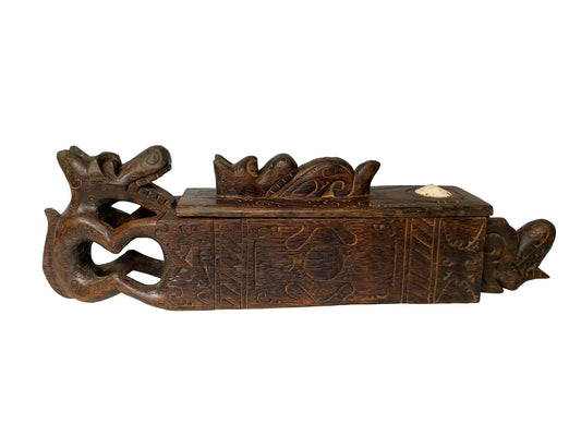 An ornate dark brown carved wooden box with relief details, featuring a dragon-like figure on the left and a small white inset on the lid, shown against a plain white background.