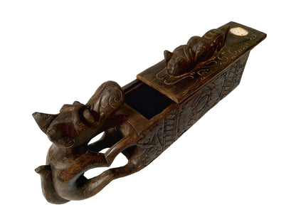A dark brown carved wooden box with dragon-like figure, featuring a sliding lid and a small handle on top, shown against a plain white background.