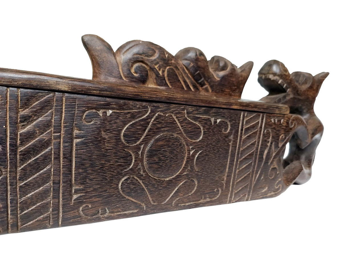 Close-up of a dark carved wooden decorative box with relief patterns and sculpted dragon-like figure on the end, shown against a plain white background.