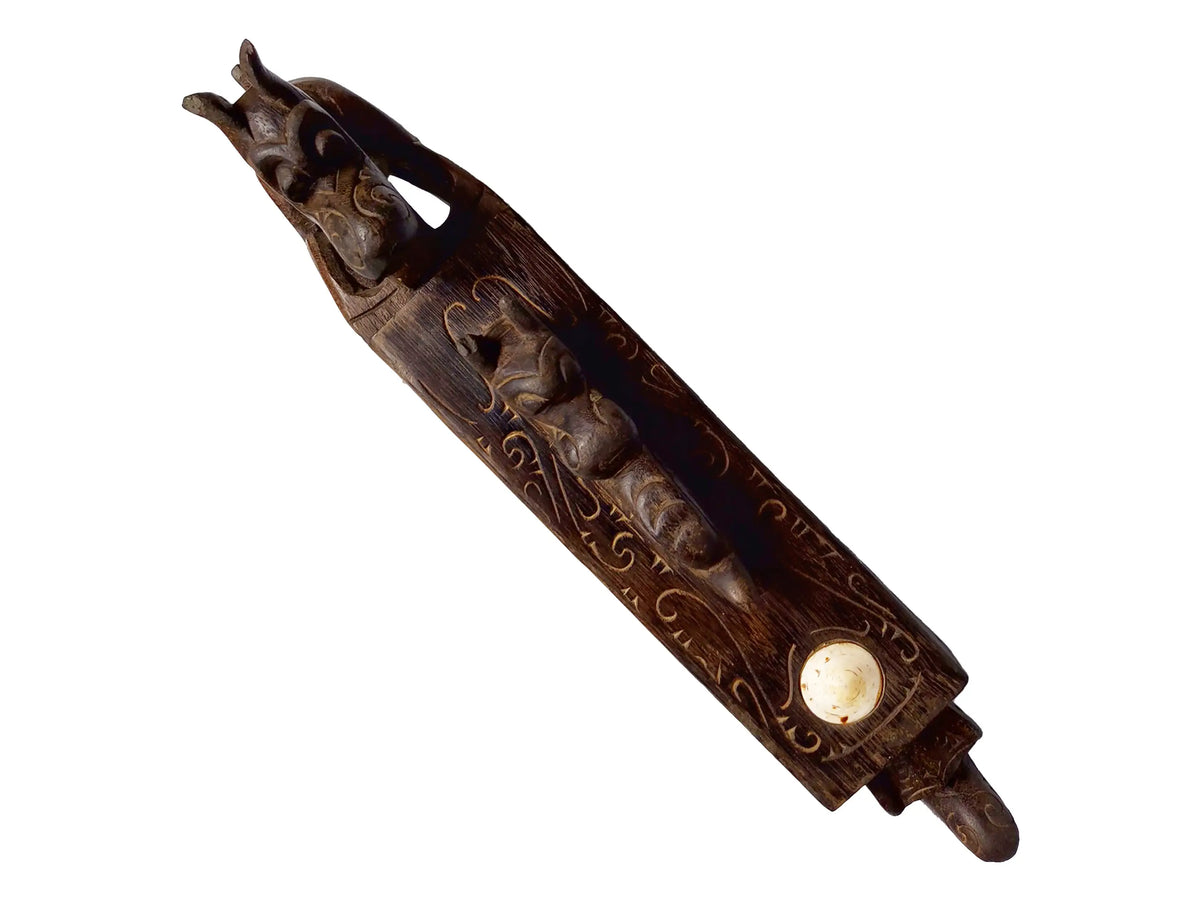 A carved wooden box, featuring engravings, a small carved animal head at one end, and a round off-white stone or shell inset near the lower right, shown on a plain white background.