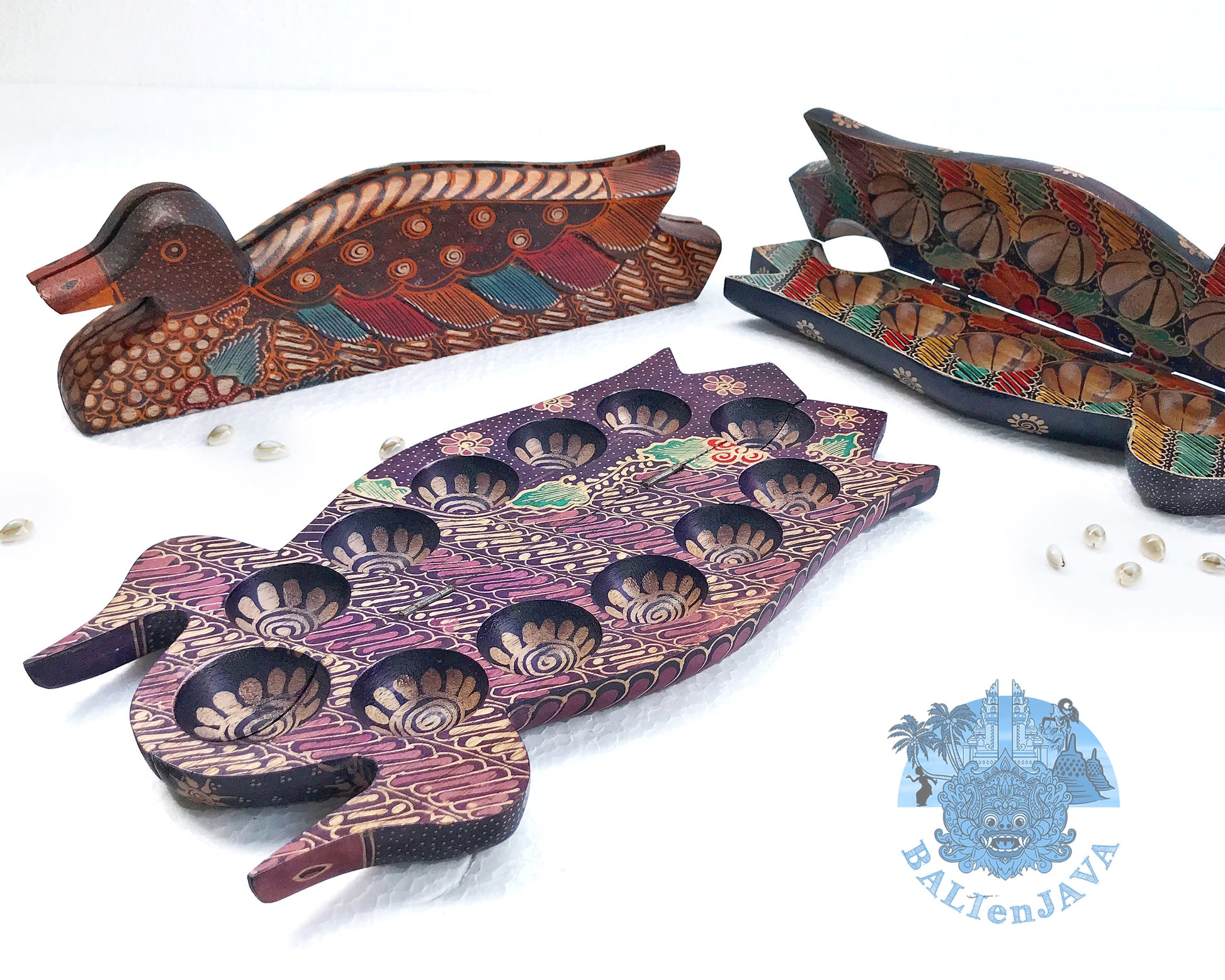 A collection of foldable wooden mancala boards in the shape of ducks with handcrafted batik patterns, along with cowrie shells scattered around.