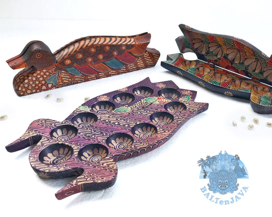 A collection of foldable wooden mancala boards in the shape of ducks with handcrafted batik patterns, along with cowrie shells scattered around.