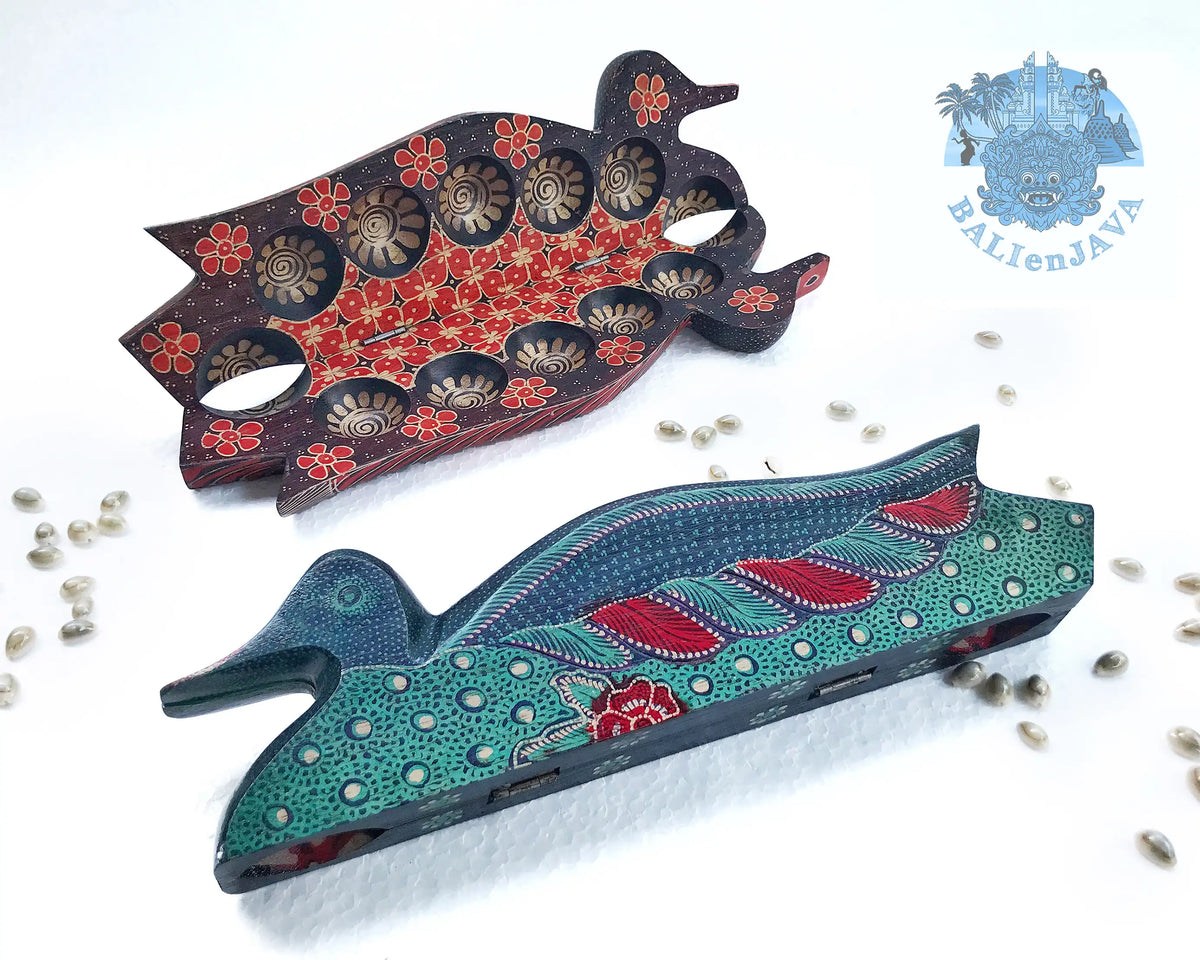 Two wooden duck board games on a white background with scattered cowrie shells. One is dark brown with red floral patterns, and the other is teal with red and green patterns.