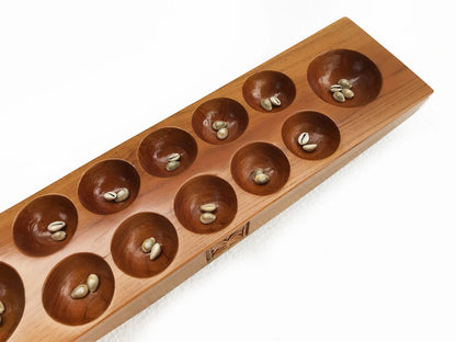 A wooden board game with ten circular holes, shown on a clean white background. Cowrie shells are placed inside the circular holes.