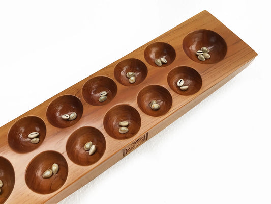 A wooden board game with ten circular holes, shown on a clean white background. Cowrie shells are placed inside the circular holes.