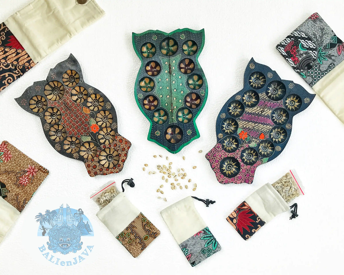 Three owl-shaped wooden mancala boards with circular pits and various colorful patterns, surrounded by fabric pouches, and cowrie shells scattered on a white background