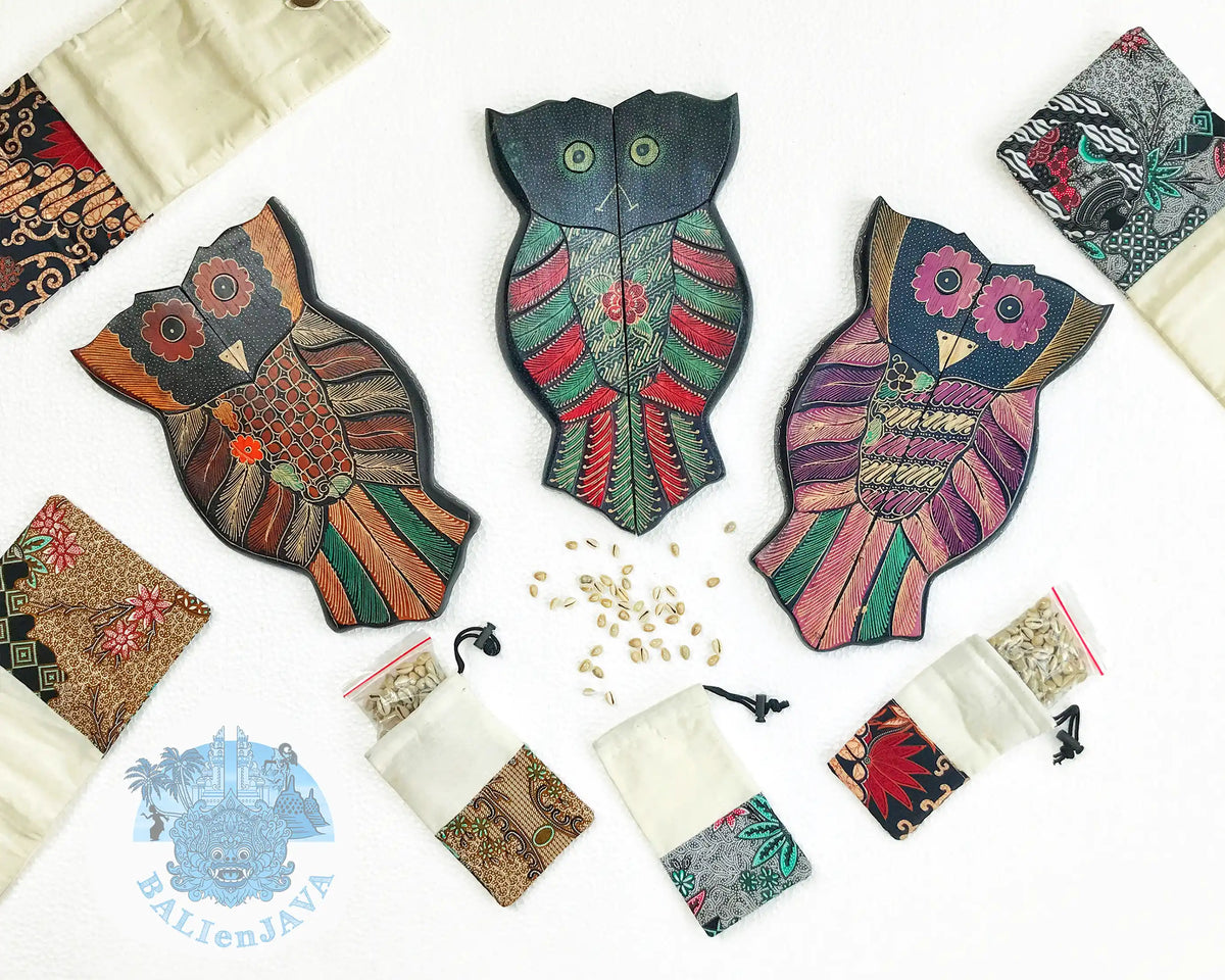 Three hand-painted wooden owl board games, displayed on a white background with small fabric pouches containing cowrie shells.