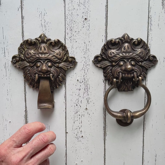 Two ornate brass door knockers with a hand knocking 